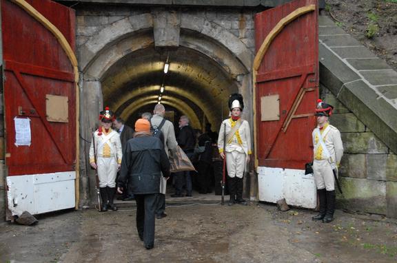 Brueckekopf_Tag_des_offenen_Denkmals. Toreingang, mit roten offen stehenden Toren, daneben drei in weiß gekleidete Personen.